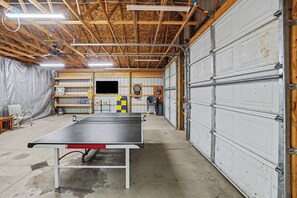 A spacious garage with a ping pong table, a dartboard, and a television. - Chase Cabin-Wi-Fi, Hot Tub, Game Room, Firepit (Chase)