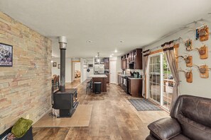 A modern kitchen with a central island, wooden cabinets, and a dining area with a brick wall. - Chase Cabin-Wi-Fi, Hot Tub, Game Room, Firepit (Chase)