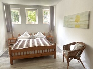 Ein Schlafzimmer mit einem hölzernen Bett, einem Sessel und drei Fenstern.