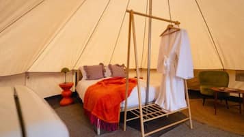 A tent with a bed, a hanging robe, and a small table.
