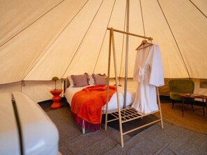 Een tent met een bed, een opbergplek voor kleding en een tafeltje.
