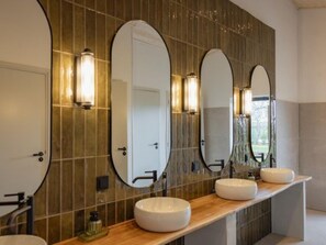 Een moderne badkamer met drie ovale spiegels, een houten wastafelmeubel en een betegelde muur.