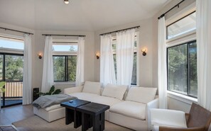 Ein geräumiges Wohnzimmer mit einem großen weißen Sofa, einem kleinen Couchtisch und Blick auf einen Balkon.
