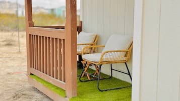 A wooden deck with two wicker chairs and a white wall.