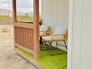 A wooden deck with two wicker chairs and a white wall.