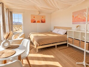 Un dormitorio con cama, escritorio, sillas, perchero y obras de arte en las paredes.