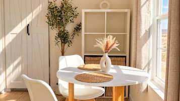 A room with a round table, two chairs, a potted plant, a vase with dried flowers, and a window with curtains.