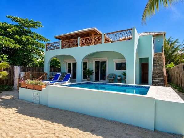 A two-story house with a swimming pool, outdoor seating, and a wooden fence. - Villa Terrapin Station in Hopkins, Beachfront, Private Pool + Rooftop Tiki Bar (Hopkins)