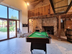 A billiards table in a room with a stone fireplace, wooden beams, and a large window. - Cottage, pets allowed - 11 guests (Saint-Paul-d'Uzore)