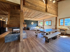 A spacious room with a high ceiling, wooden beams, a stone fireplace, and a large dining table with benches. - Semi-detached chalet with Giffre valley view (Samoëns)