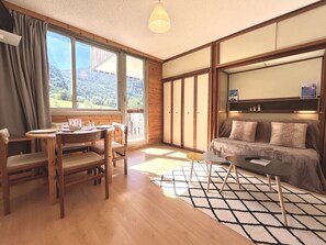 A room with a dining table, chairs, a sofa, and a view of a mountainous landscape through large windows. - Studio with slope view - 6 guests (La Salle-les-Alpes)