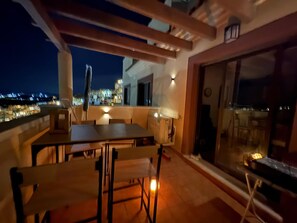 Ein Außenbereich mit Sitzgelegenheiten, Tisch, Stühlen, einer Pergola und Blick auf die beleuchtete Stadt.