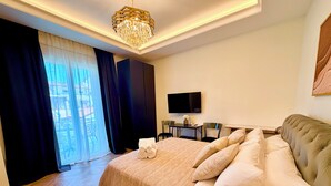 Ein Hotelzimmer mit einem großen Bett, einem Fernseher, einem Schreibtisch und Blick durch ein Fenster.