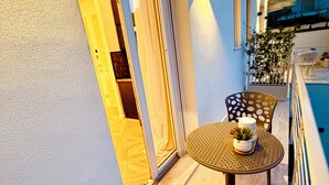 Ein Balkon mit rundem Tisch, zwei Stühlen, einer Schiebetür aus Glas und einem kleinen Blumentopf.