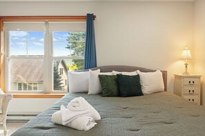 A bedroom with a bed, a nightstand, a lamp, and a view of the outside. - Rustic 3BR Condo - Fireplace - Tannersville (Tannersville)