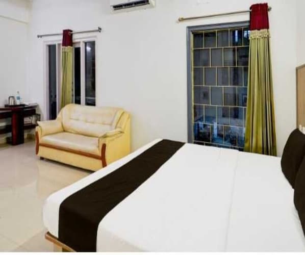 A hotel room with a bed, a sofa, a window with curtains, and a radiator. - Suite Aysha Stay Inn (Kodaikanal)