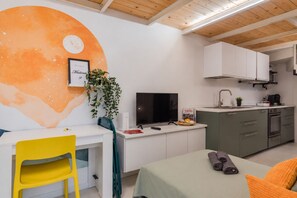 Ett kompakt boendeutrymme med en matplats, ett litet kök och en säng med hoprullade handdukar.
