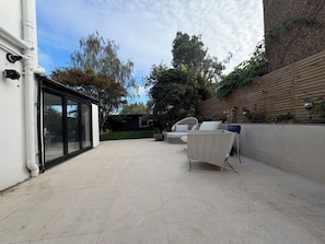 An outdoor patio area with a tiled floor, a white wall with a sliding glass door, and a wooden fence. - Boutique Stays - is a luxury hideaway in the Greenwich borough of London (Greater London)