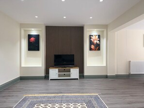 A modern living room with a flat-screen TV on a wooden cabinet, flanked by two wall-mounted paintings, a patterned rug, and a radiator. - The Croydon Hideaway - Newly decorated 4 (Croydon)