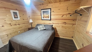 Una stanza con rivestimenti in legno, un letto, un quadro incorniciato e un attaccapanni.