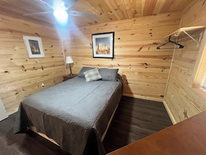Ein Zimmer mit Holzwänden, einem Bett, einem gerahmten Bild und einem Kleiderhaken.