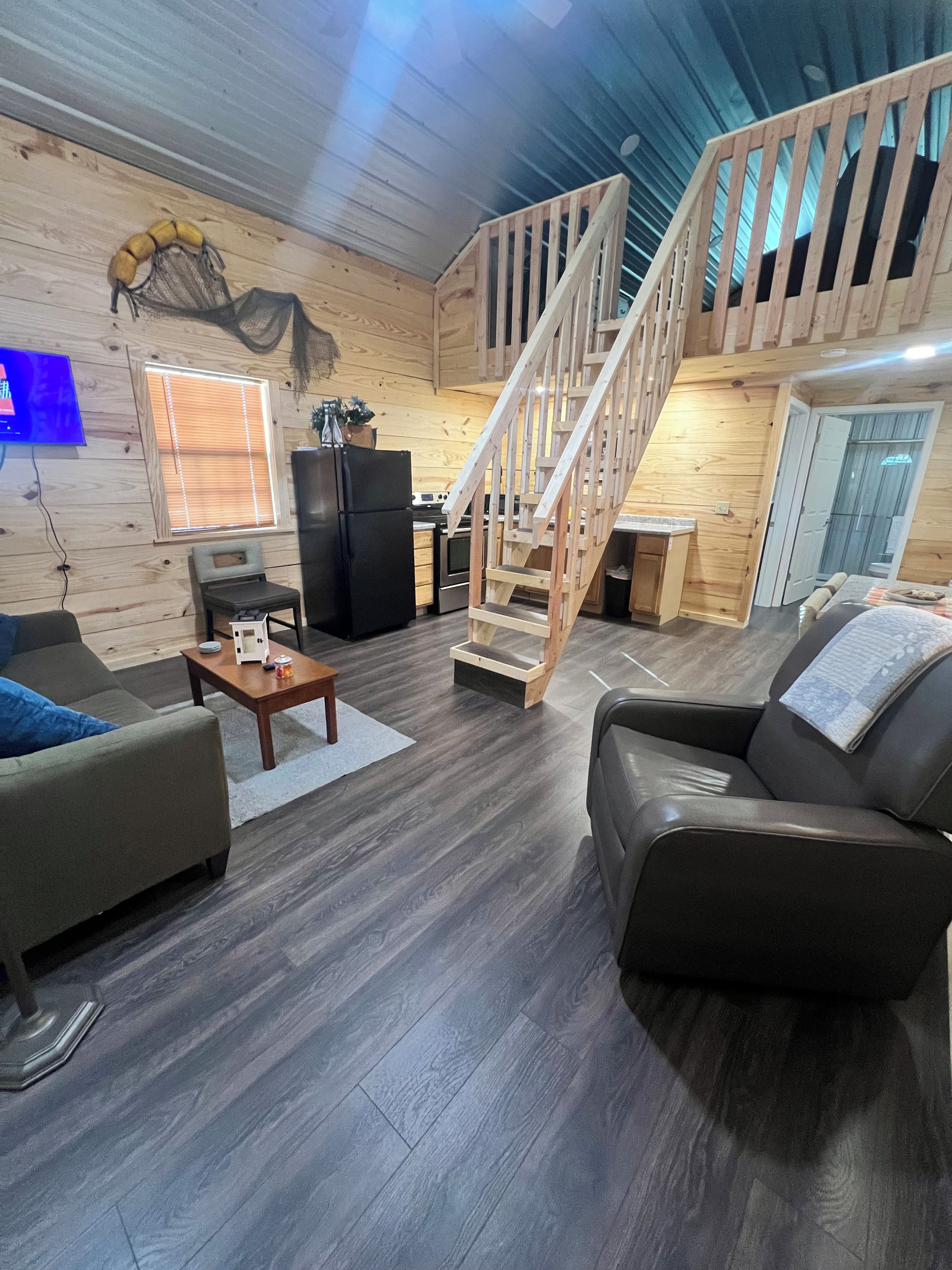 A spacious living area with a wooden staircase, a kitchen, and a seating area with a sofa and armchair.
