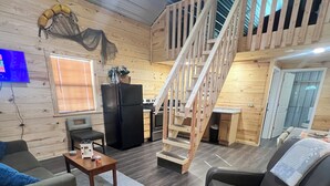 Un'ampia zona giorno con una scala in legno, una cucina e un angolo salotto con divano e poltrona.