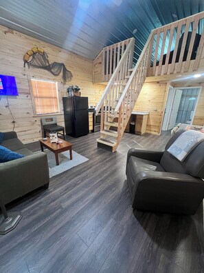 Ein geräumiger Wohnbereich mit einer Holztreppe, einer Küche und einer Sitzecke mit Sofa und Sesseln.