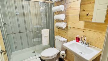 Une salle de bain avec une douche à parois de verre, des toilettes, un lavabo avec un miroir et un porte-serviettes avec des serviettes.