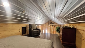 Una stanza con soffitto spiovente, camino, un letto, una poltrona e un comò.