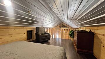 A room with a sloped ceiling, a fireplace, a bed, a chair, and a dresser.