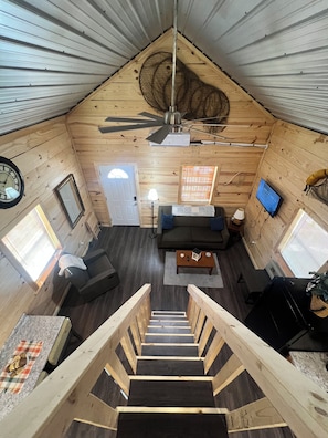 A wooden interior with a ceiling fan, a sofa, a coffee table, a TV, and a staircase.