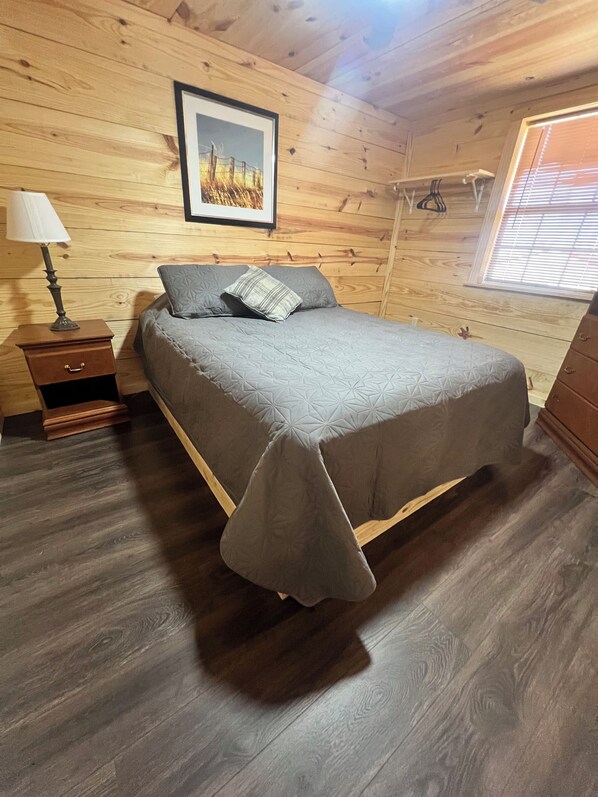 A room with a bed, a nightstand, a lamp, and a window with blinds.