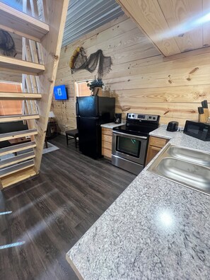 A kitchen with a built-in oven, microwave, and a sink. There is a wooden bench with a TV mounted on the wall.
