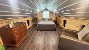 A cozy attic bedroom with a sloped ceiling, wooden walls, a bed, a dresser, and a chair.