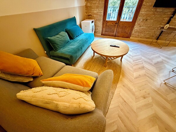 A living room with a sofa, a small round table, and a herringbone floor pattern. - Apartment near the Sagrada Familia (Barcelona)