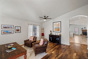 A spacious living room with hardwood flooring, a ceiling fan, and a fireplace.