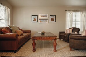 A living room with a brown leather sofa, a wooden coffee table, and a brown armchair. There are three framed pictures on the wall. - 4 Bedroom house with pool, putting green, and chef's kitchen! (Glendale)