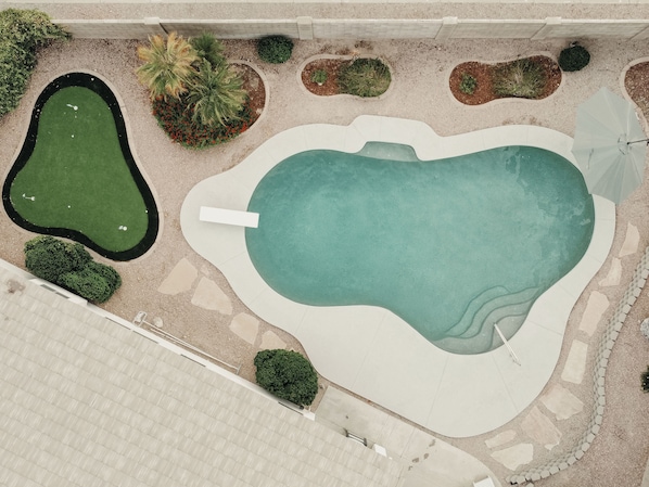Piscina com deck ao redor, pequena área de jardim com diversas plantas e um caminho pavimentado que leva à piscina.