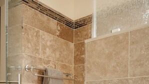 Un área de ducha con puerta de vidrio, paredes con azulejos y un perchero para toallas.