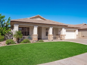 A residential house with a covered porch, a garage, and a well-maintained lawn.