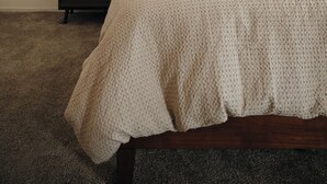 Un dormitorio con cama, almohadas, una mesita de noche y suelo alfombrado.