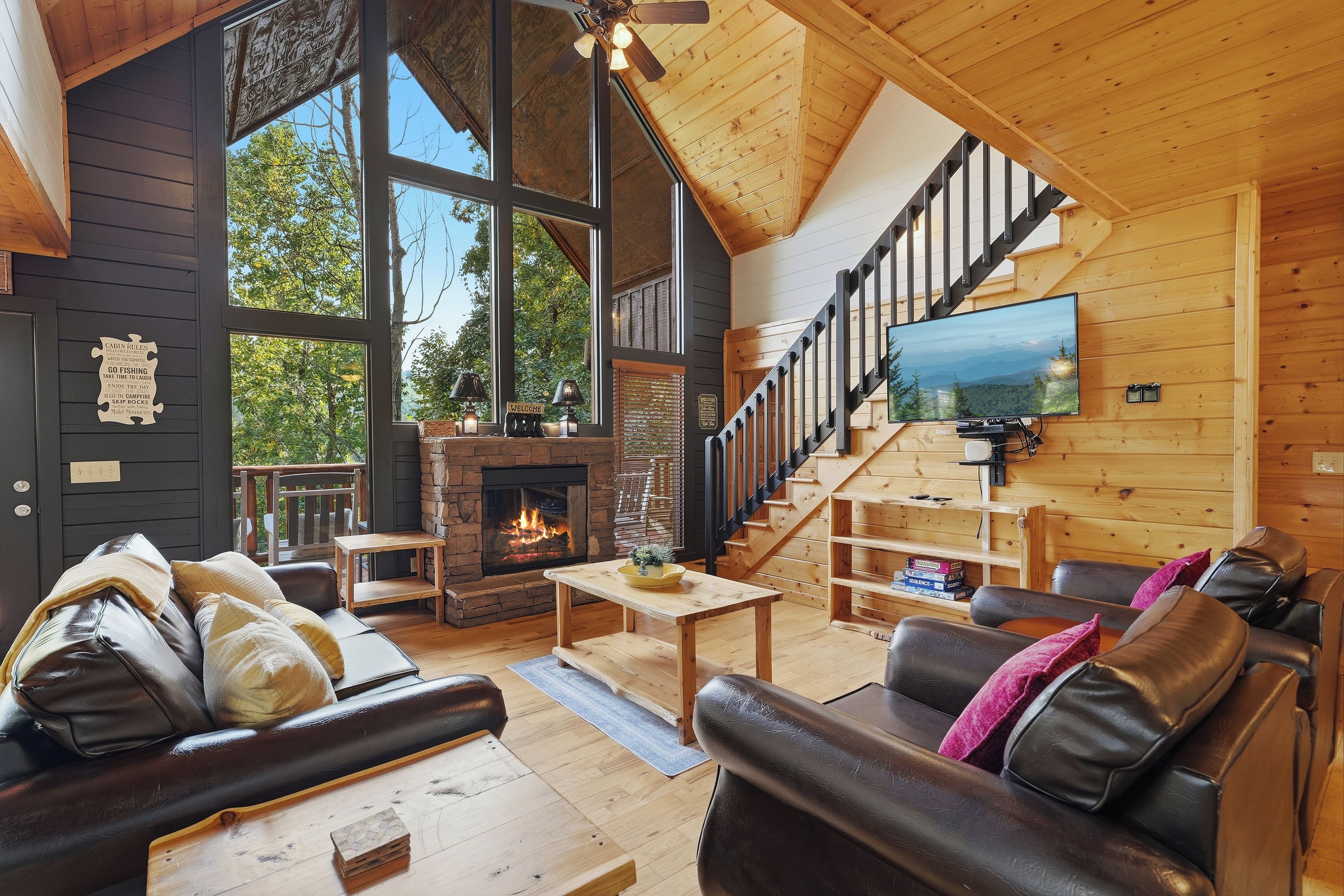 Interior acogedor de una cabaña con chimenea, sofás de cuero, un televisor montado en la pared y una escalera que sube a un nivel superior.