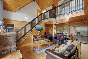 A spacious living area with a wooden staircase, leather sofas, a stone fireplace, and a large window. - Big Bear Estate. 1 mile to Dollywood! (Sevierville)
