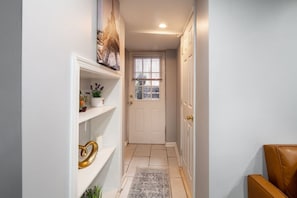 A hallway with a white door, shelves with decorative items, and a rug.