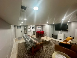 A living room with a sofa, a coffee table, a TV, and a dining area with a red tablecloth.