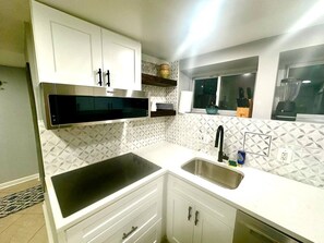 A modern kitchen with white cabinetry, a black stovetop, a stainless steel sink, and a patterned backsplash. - Cozy 2 BR Basement Suite (Washington)