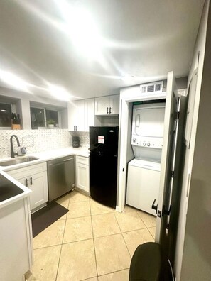 A compact kitchen with white cabinets, a black refrigerator, a washing machine, and a dishwasher.