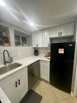 A kitchen with white cabinets, a black refrigerator, a dishwasher, and a window.