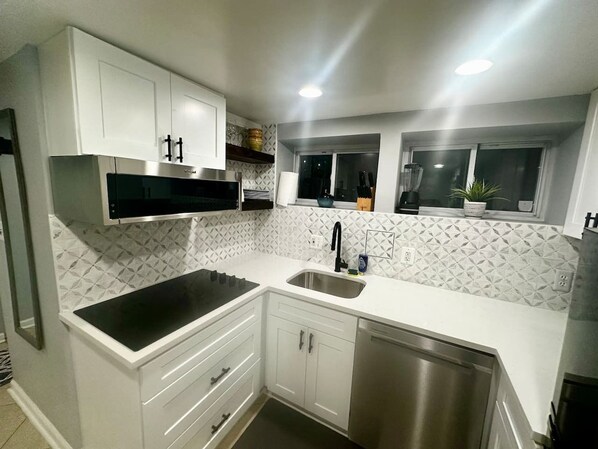 A modern kitchen with white cabinetry, a black countertop, and a stainless steel sink.